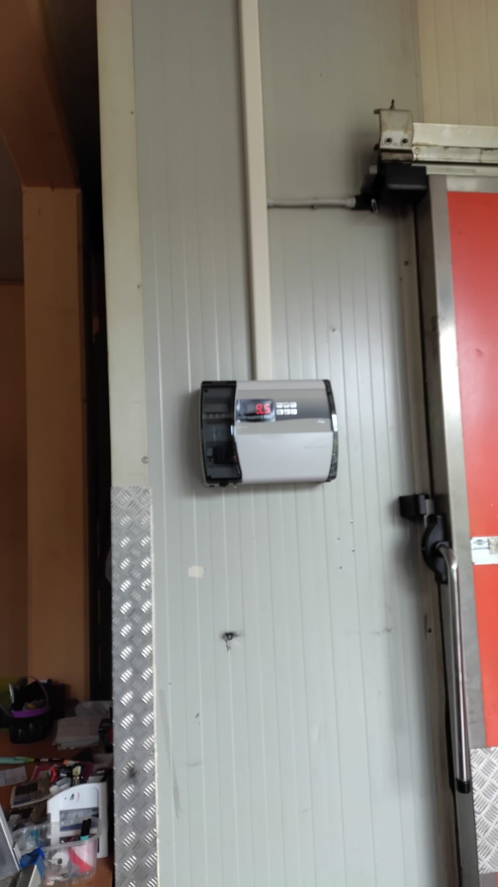 Porta di cella frigorifera con quadretto di comando e portone rosso sullo sfondo